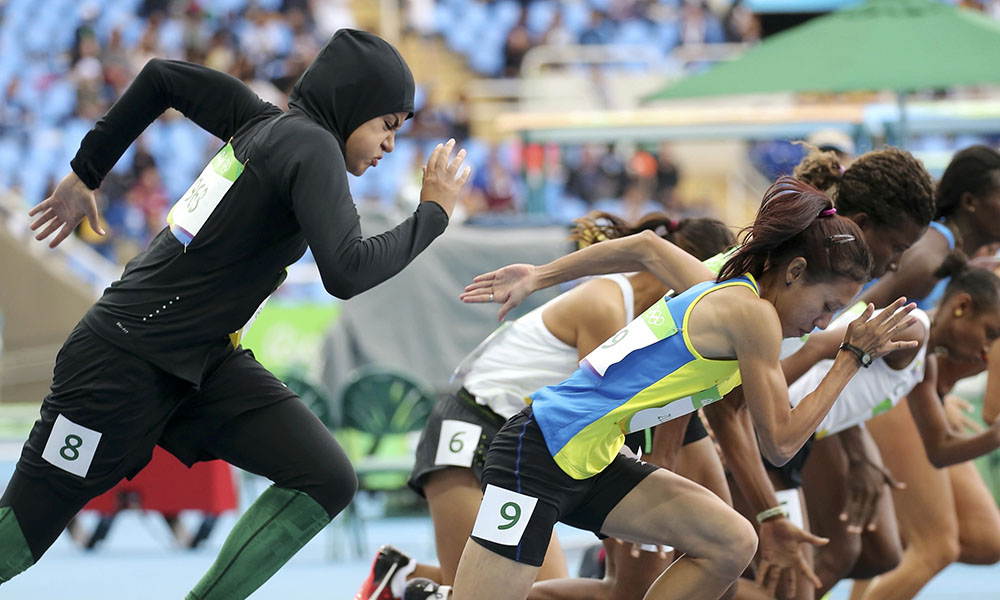 尽情地伸展身体，专注地瞄准目标，这些戴着头巾的女运动员，来自阿拉伯世界，她们在奥运会场里展现穆斯林女性的运动精神。图为2016里约奥运女子100米预赛沙特选手Kariman Abuljadayel。她是该国第一名参加该比赛的选手，赛场上她的穿着与身边的对手形成鲜明对比。