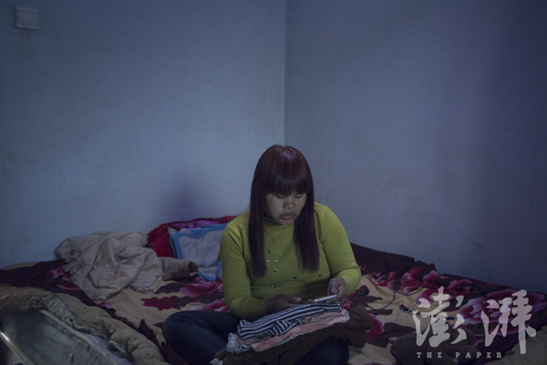 2016年3月29日，Sophorn坐在床上一边叠衣服一边玩手机。她正在收拾要带回柬埔寨的行李。本文图片丛妍澎湃新闻记者陈荣辉图