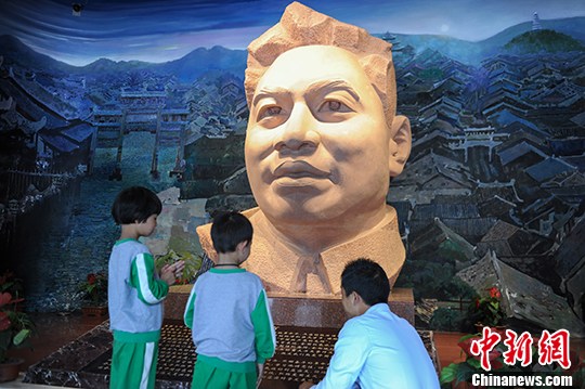 图为两位小朋友在雕像前听父亲讲解王若飞事迹。 中新社记者 贺俊怡 摄