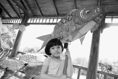 休闲鱼庄里，一个女孩举着鱼灯玩耍。