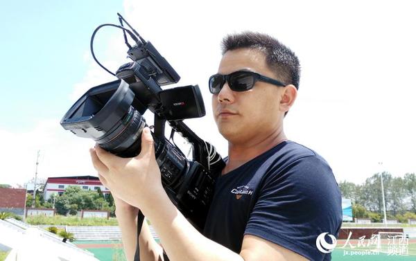 烈日下,陈艳伟手持摄像机在采访拍摄.