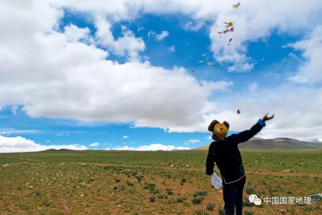 一位村民,冲着雪山,向着天空,撒出许愿的风马.